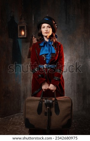 A stylish lady in a burgundy old-fashioned suit with a hat and a valise. Brunette in a retro style suit Royalty-Free Stock Photo #2342680975