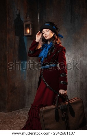 A stylish lady in a burgundy old-fashioned suit with a hat and a valise. Brunette in a retro style suit Royalty-Free Stock Photo #2342681107