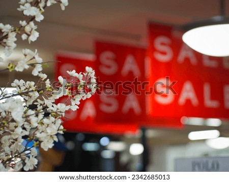 A few branches of the white cherry blossoms flowers is prominently framed against blurred background of several bright red 'sale' signages.