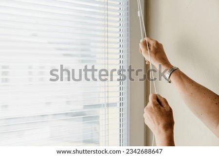 The woman opens and closes the horizontal white blinds with her hands. Windows jalousie Royalty-Free Stock Photo #2342688647