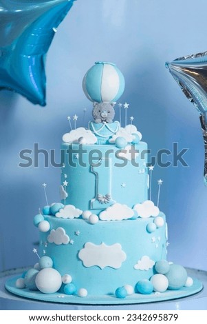 two tiered blue first birthday cake decorated with balloons and stars with a bear