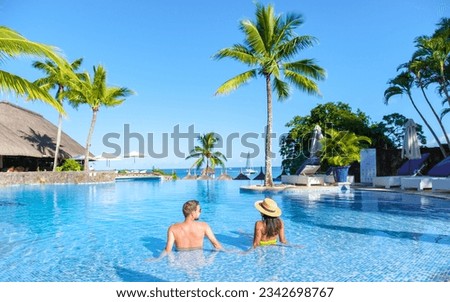 Man and Woman relaxing in a swimming pool, a couple on a honeymoon vacation in Mauritius tanning in the pool with palm trees and sun beds Royalty-Free Stock Photo #2342698767