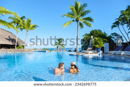 Man and Woman relaxing in a swimming pool, a couple on a honeymoon vacation in Mauritius tanning in the pool with palm trees and sun beds Royalty-Free Stock Photo #2342698775
