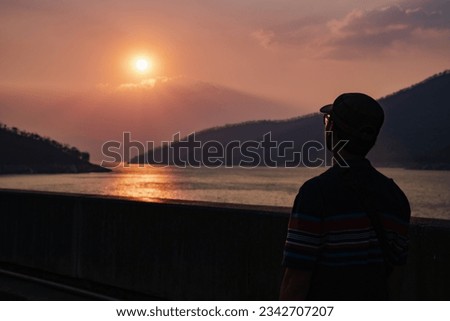 Thesilhouette of a man standing looking at the scenery of lakes and mountains at the time when the sun was about to set.