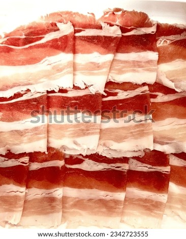 a photography of a plate of bacon strips on a table, bacon strips on a plate with a knife.