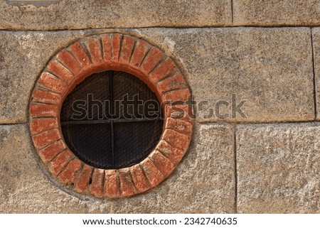 Close-up of a small round window with brick frame and iron security bars. Small village of Framura, La Spezia province, Liguria, Italy, Europe. Royalty-Free Stock Photo #2342740635