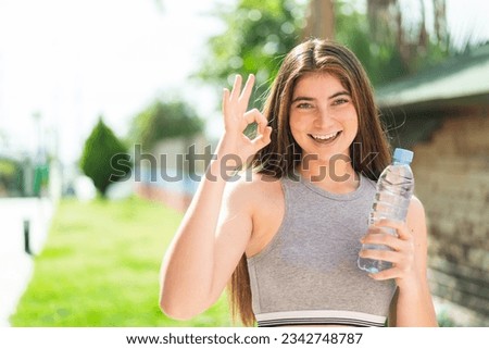 Young pretty caucasian woman with a bottle of water at outdoors showing ok sign with fingers