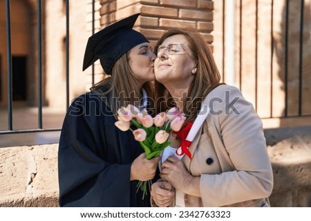 Mother and daughter hugging each other celebrating graduation holding diploma and flowers at university