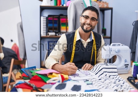 Young arab man tailor smiling confident drawing on notebook at clothing factory