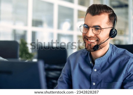 Technical support operator working with headset in office. Smiling handsome man working as call centre operator, speaking to customer. Happy businessman working remotely while doing video conference. Royalty-Free Stock Photo #2342828287