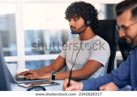 Call center employee accompanied by his team. Focused support operator at work. Young employee working with headset and laptop. Royalty-Free Stock Photo #2342828317