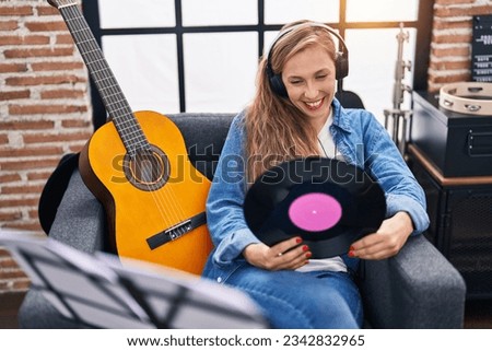 Young blonde woman musician listening to music holding vinyl disc at music studio
