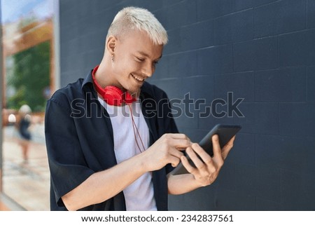 Young caucasian man using touchpad wearing headphones at street