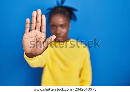 Beautiful black woman standing over blue background doing stop sing with palm of the hand. warning expression with negative and serious gesture on the face. 