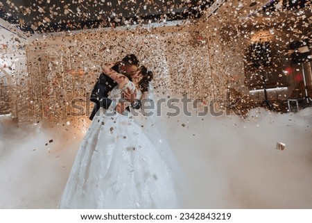 Gorgeous bride and stylish groom dancing under golden confetti at wedding reception. Happy wedding couple performing first dance in restaurant. Romantic moments Royalty-Free Stock Photo #2342843219