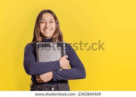Portrait of a female student with books isolated on yellow background with copy space.