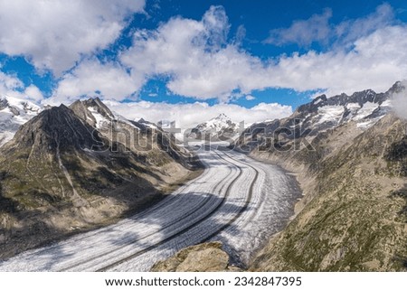 An aerial view of a snowy trail through rugged mountains under a bright sky in Valais, Switzerland Royalty-Free Stock Photo #2342847395