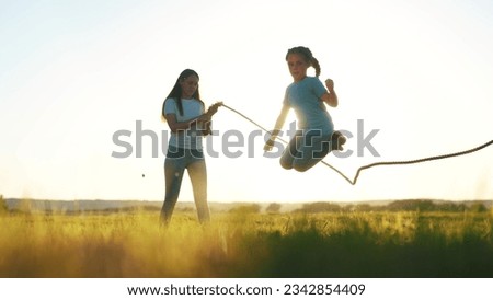 children in the park playing rope jumping. happy family kid dream concept. little girl jumping over big jump rope joint play children silhouette outdoors in the park lifestyle Royalty-Free Stock Photo #2342854409