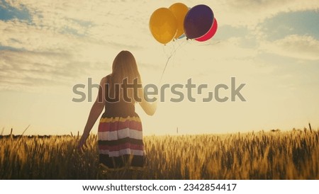 little girl with balloons runs at sunset through field of wheat at sunset. holiday birthday. happy family kid dream concept. girl with long hair runs with balloons silhouette in park fun field