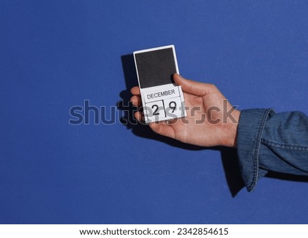 Man's hand in denim shirt holds wooden block calendar organizer with date December 29 on a blue background