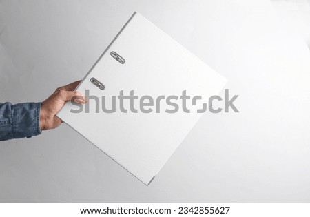 Man's hand in denim shirt holding white ring folder on gray background Royalty-Free Stock Photo #2342855627