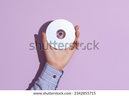 Man's hand in shirt holding cd disk on purple pastel background with shadow.