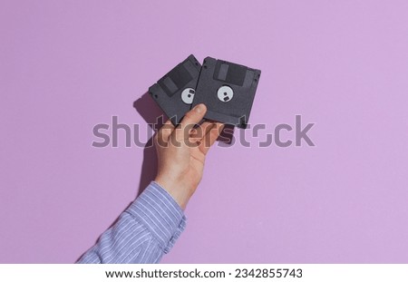 Man's hand in shirt holding black floppy disks on purple pastel background with shadow Royalty-Free Stock Photo #2342855743