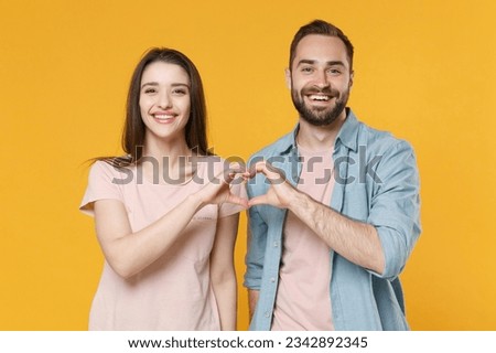 Smiling young couple two friends man woman in pastel blue casual clothes isolated on yellow background. People lifestyle concept. Mock up copy space. Showing shape heart with hands, heart-shape sign