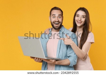 Excited young couple friends man woman in pastel blue casual clothes posing isolated on yellow background. People lifestyle concept. Mock up copy space. Pointing index finger on laptop pc computer