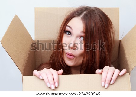 Beautiful girl looks out of a cardboard box. Lightweight, easy to move. Emotions concept. Unexpected gift concept Royalty-Free Stock Photo #234290545