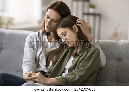 Compassionate young mother comforting depressed sad teen girl, hugging daughter with love, care, speaking, giving sympathy, advice, support, holding kids hand, sitting on home couch Royalty-Free Stock Photo #2342909035