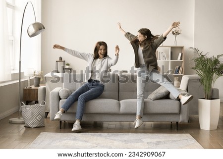 Cheerful mom and excited teenager kid hitting couch at home, jumping, flying in air, throwing bodies on soft comfortable sofa, screaming, laughing, having fun, playing active games, Full length Royalty-Free Stock Photo #2342909067