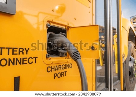 Yellow electric school bus plugged in at a charging station. Royalty-Free Stock Photo #2342938079