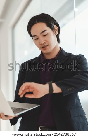 Portrait of successful asian business man using laptop computer working online, planning project, checking time waiting in modern office. Smart businessman at workplace, technology business concept