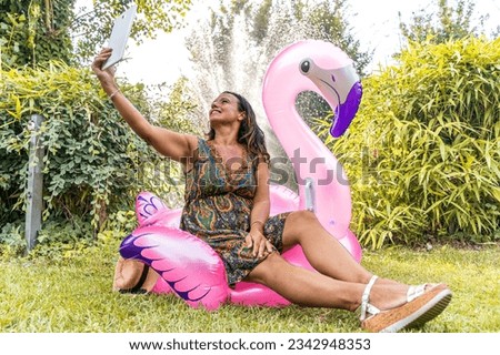 beautiful smiling middle aged woman taking a selfie sitting on a pink flamingo shaped inflatable toy