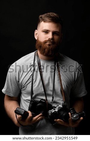 Photographer in grey t-shirt with a bunch of different vintage old film cameras looks into the camera. Close up portrait of man holding vintage camera. Film photography.