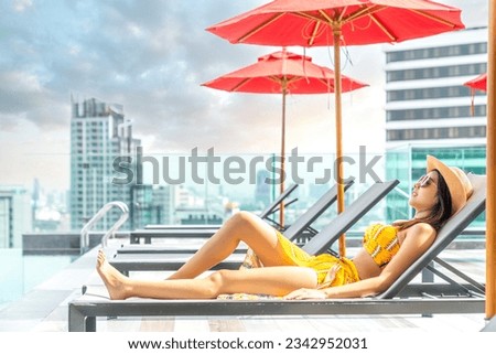 Asian traveller woman sleep and relax at swimming pool on hotel roof top with Bangkok city view, Thailand