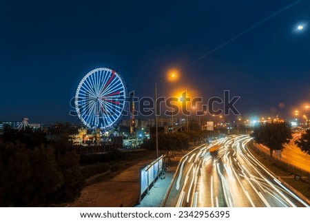 Amusement park at night. bright lights on the Ferris wheel. Long exposure lights from cars.
