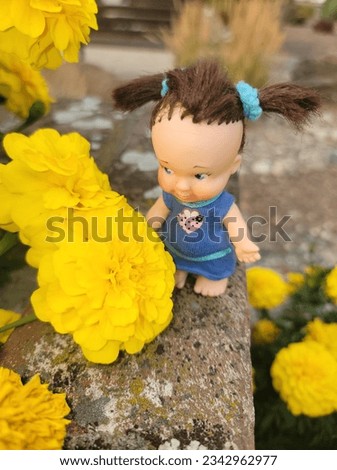 A cute little doll looking at large yellow flowers
