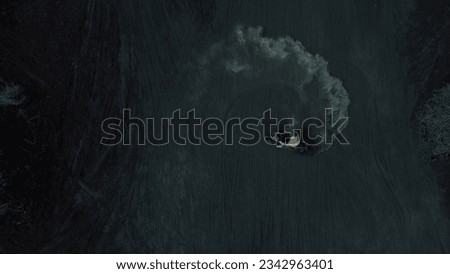 A young man drifts on a motorcycle on black volcanic lava, top view. Drift on volcanic sand, clouds of sand rise. Spectacular stunts on a motorcycle in the sand. Royalty-Free Stock Photo #2342963401