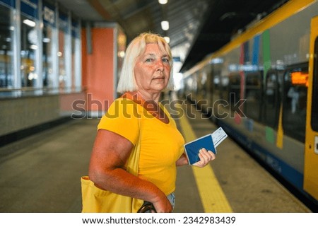 Happy 50s senior woman biometric passport and train ticket waiting train on station platform. Travel to vacation by fast train.High quality photo