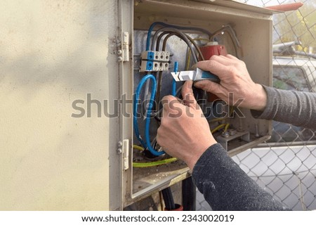 Electrician work process outdoors. hands of an electrician close-up clean the insulation from the wire with a special knife. An electrician connects wires in a shield with copy space. Royalty-Free Stock Photo #2343002019