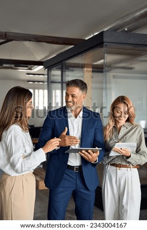 Group of diverse partners mature Latin business man and European business women discussing project on tablet in office. Team of colleagues professionals business people working together, vertical.