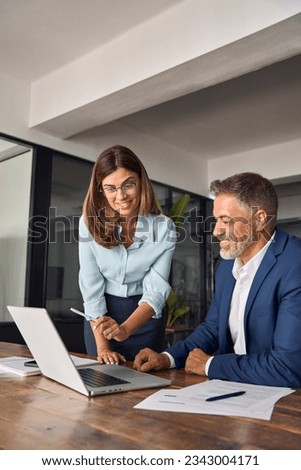 Vertical shot of diverse partners mature Latin businessman and European businesswoman discussing project on laptop at table in office. Two colleagues of professional business people working together. Royalty-Free Stock Photo #2343004171