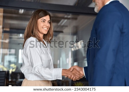 Mature Latin business team of woman and European business man shaking hands as colleagues, partners or employees, signing a contract. Group of people satisfied with results of team work together.