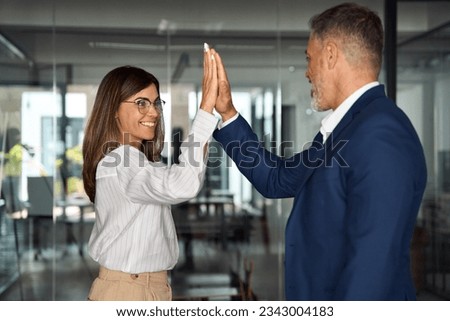 Team of mature Latin business woman and European business man doing high five while discussing project in office. Team of colleagues, partners satisfied with results of team work on project together. Royalty-Free Stock Photo #2343004183