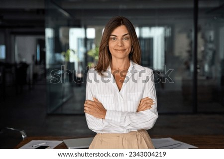 Beautiful hispanic senior business woman with crossed arms smiling at camera. European or latin confident mature good looking middle age leader female businesswoman on office background, copy space. Royalty-Free Stock Photo #2343004219