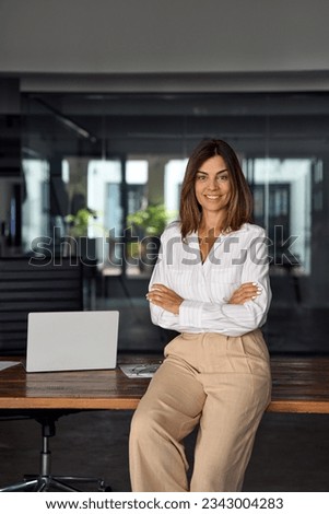 Vertical photo of Hispanic business woman with crossed arms smiling at camera. European or latin confident mature good looking middle age leader female businesswoman on office background, copy space.
