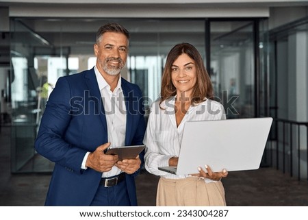 Two diverse partners, colleagues, team of confident professional business people work together. Mature Latin business man and European business woman working on project using digital gadget in office. Royalty-Free Stock Photo #2343004287