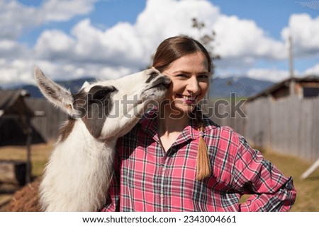 Young woman in shirt standing next to white llama at zoo on a sunny day, smiling, posing for picture